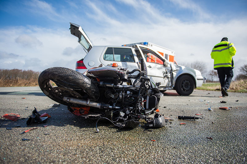 A motorcycle-involved traffic accident resulting in a mangled motorcycle and damaged hatchback vehicle with ambulance on scene and tow operator on a rural Lehigh Valley road.