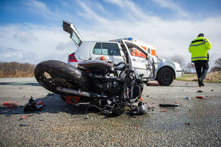 Wreckage of a motorcycle after colliding with a car, with tow truck operator walking through scene.