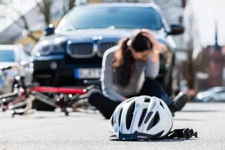 A female bicyclist sits injured and in pain on a Lehigh Valley road in front of a BMW SUV with her helmet laying in the foreground.